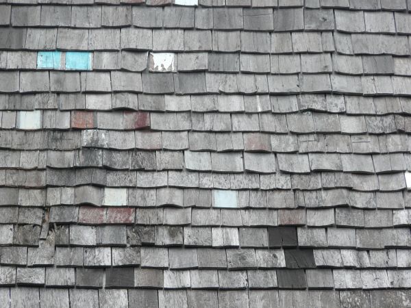 Old roof texture with worn grey shingles and few shingles of random color.